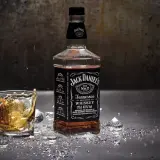 Butelka i szklanka Jack Daniel's na metalowym blacie, z lodem i błyszczącymi drobinkami. Czy whisky jest zdrowe? To pytanie pozostaje otwarte.