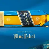 Elegancka butelka Johnnie Walker Blue Label leży na niebieskim tle. Złoty płyn i niebieskie szkło tworzą luksusowy kontrast.