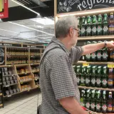 Starszy mężczyzna wybiera piwo bezalkoholowe, zastanawiając się, czy piwo bezalkoholowe podnosi cukier. Na półkach widać różne rodzaje piw.