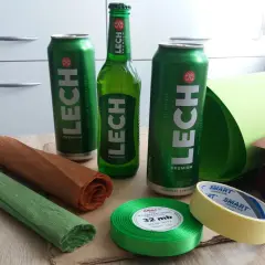 Materiały do kreatywnego pakowania piwa na prezent: puszki i butelka Lecha, kolorowe papiery, wstążka i taśma.