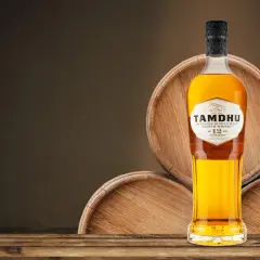 Butelka whisky single malt Tamdhu 12 lat, stojąca na drewnianych beczkach.