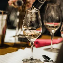 Jak zaplanować degustację wina w domu dla grupy znajomych? Nalewanie białego wina do kieliszków, przygotowanie stołu.