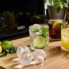 Jak dobrać lód do drinka: kostki, kule czy lód suchy? Na stole cytryny, limonki, drinki i różne rodzaje lodu.