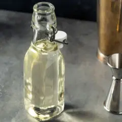 Domowy syrop cukrowy (simple syrup) w butelce, obok jigger i shakera. Idealny do drinków, łatwy do przygotowania krok po kroku.