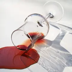 Przewrócony kieliszek z czerwonym winem na białym obrusie. Szukasz jak usunąć plamy z czerwonego wina z białego obrusa skuteczne metody?