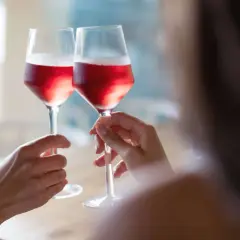 Dwie osoby wznoszą toast kieliszkami z różowym winem. Czy wino różowe powstaje z mieszania białego z czerwonym? Proces produkcji jest ciekawy!