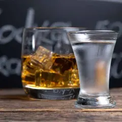Szklanka whisky z lodem i kieliszek mroźnej wódki na drewnianym stole. Co jest mocniejsze wódka czy whisky?