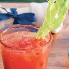 Jak przygotować infuzję wódki z chrzanem do krwawej mary? Szklanka z drinkiem i łodygą selera, na drewnianym stole.