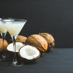 Dwa kieliszki z kremowym drinkiem z malibu, otoczone świeżymi kokosami, tworzą tropikalną atmosferę.