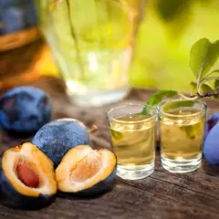 Jak przygotować domową nalewkę na whisky z suszonymi śliwkami? Dojrzałe śliwki i dwa kieliszki złocistego trunku na drewnianym stole.