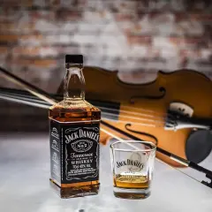 Butelka Jack Daniel's i szklanka z whisky na tle skrzypiec. Czy koniak i whisky to to samo? Nie, to dwa różne trunki.