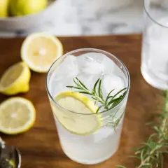 Orzeźwiający gin z tonikiem z plasterkiem cytryny i gałązką rozmarynu, otoczony świeżymi cytrynami.