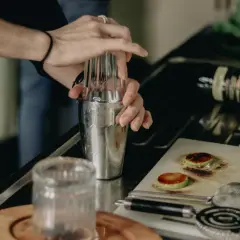 Ręce barmana mieszają składniki w shakerze, by uzyskać idealne rozcieńczenie. Na blacie leży butelka whisky.