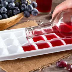 Czy warto mrozić wino do późniejszego wykorzystania w kuchni? Czerwone wino wlewane do pojemnika na lód, obok kiści winogron.