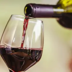 Czerwone wino nalewane do kieliszka. Widoczne "łzy" na ściance, świadczące o zawartości alkoholu.