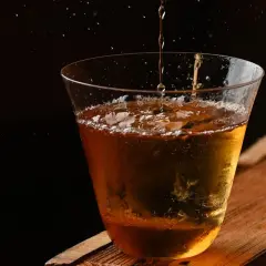 Jak przygotować Penicillin – nowoczesny klasyk z miodem i imbirem. Bursztynowy płyn z lodem w szkle, w tle ciemność.