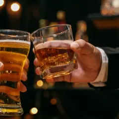 Dwie ręce unoszą kieliszki: jeden z piwem, drugi z whisky. Dyskusja: co jest zdrowsze whisky czy wódka?