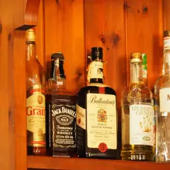 Butelki whisky na drewnianej półce. Zwróć uwagę na zmętnienie i osad w starych butelkach, by rozpoznać objawy zepsutej whisky.