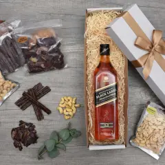 Jak przygotować prezentowy zestaw whisky dla początkującego konesera: butelka Johnnie Walker Black Label, suszone mięso, orzechy i eleganckie pudełko.