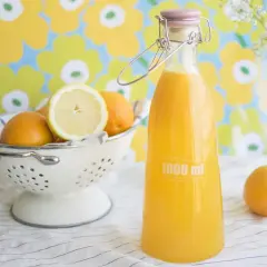 Świeżo wyciśnięty sok pomarańczowy w butelce, obok pomarańczy i cytryny w sitku. Jak dbać o świeżość owoców, by uniknąć objawów sfermentowanego soku w barze.