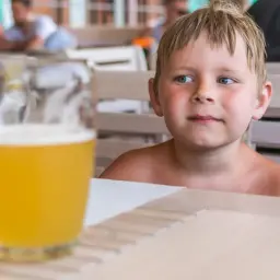 Chłopiec z zaciekawieniem patrzy na kufel piwa bezalkoholowego. Czy dzieci mogą pić piwo bezalkoholowe?