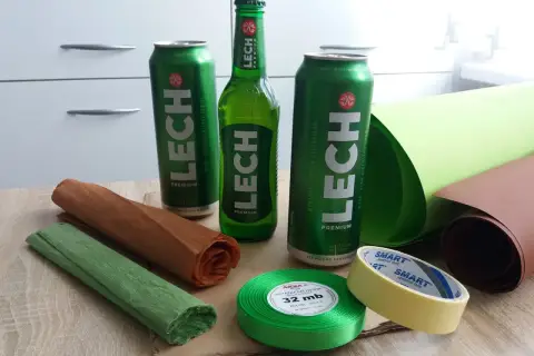 Materiały do kreatywnego pakowania piwa na prezent: puszki i butelka Lecha, kolorowe papiery, wstążka i taśma.