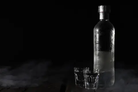 Chłodna wódka w butelce i kieliszkach, otoczona mgiełką. Czy otwarta wódka traci procenty? Tajemnica nocy.