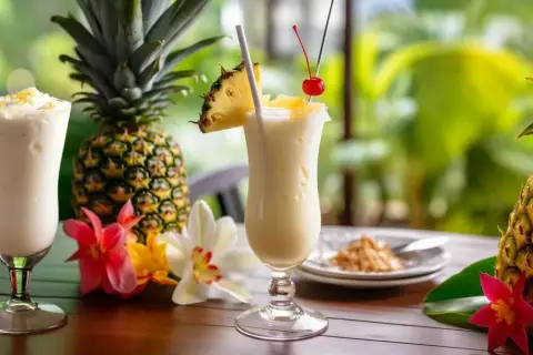Dwa orzeźwiające drinki pina colada z ananasem i wisienką, otoczone świeżymi ananasami i tropikalnymi kwiatami.