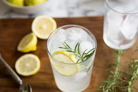 Orzeźwiający gin z tonikiem z plasterkiem cytryny i gałązką rozmarynu, otoczony świeżymi cytrynami.