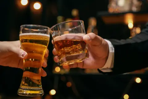 Dwie ręce unoszą kieliszki: jeden z piwem, drugi z whisky. Dyskusja: co jest zdrowsze whisky czy wódka?