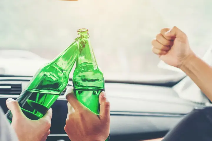 Dwie osoby w samochodzie wznoszą toast zielonymi butelkami piwa. Pytanie brzmi: ile piw można wypić przed jazdą?