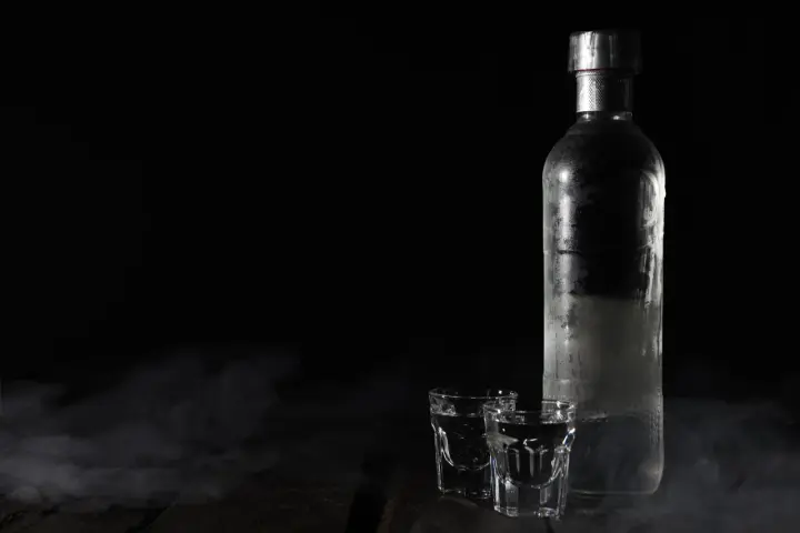 Chłodna wódka w butelce i kieliszkach, otoczona mgiełką. Czy otwarta wódka traci procenty? Tajemnica nocy.