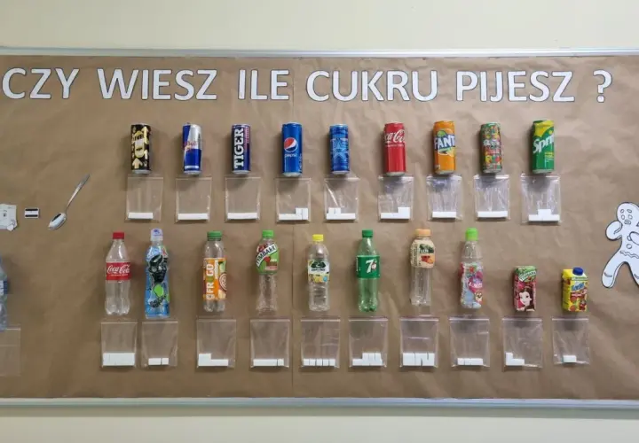 Tablica edukacyjna pokazuje, ile cukru jest w popularnych napojach. Obok każdej butelki i puszki znajduje się woreczek z odpowiadającą ilością kostek cukru.