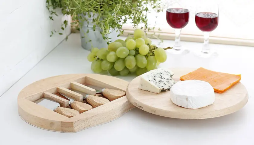 Jak przygotować deskę serów do wina: dobór smaków i tekstur. Ser pleśniowy, brie i cheddar z winogronami i kieliszkami wina.