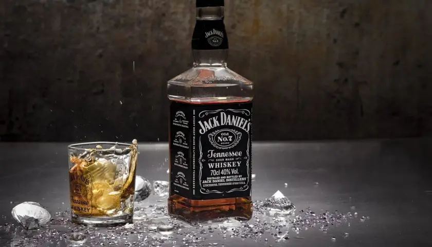 Butelka i szklanka Jack Daniel's na metalowym blacie, z lodem i błyszczącymi drobinkami. Czy whisky jest zdrowe? To pytanie pozostaje otwarte.