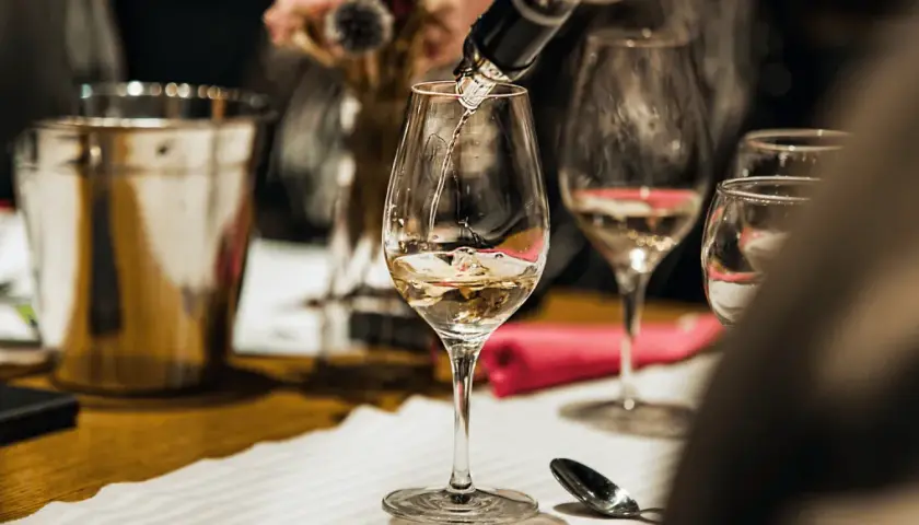 Jak zaplanować degustację wina w domu dla grupy znajomych? Nalewanie białego wina do kieliszków, przygotowanie stołu.