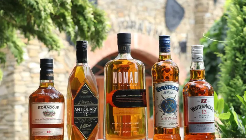Jak odczytać etykietę szkockiej whisky: Islay, Highlands, Speyside. Pięć butelek whisky na drewnianym stole.