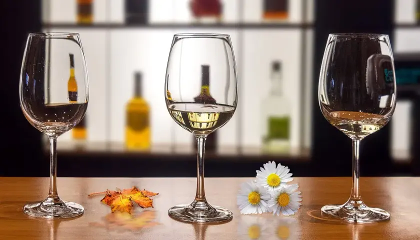 Trzy kieliszki na drewnianym blacie. Jak usunąć zapach alkoholu z kieliszka przed ponowną degustacją? Jesienne liście i kwiaty dodają uroku.
