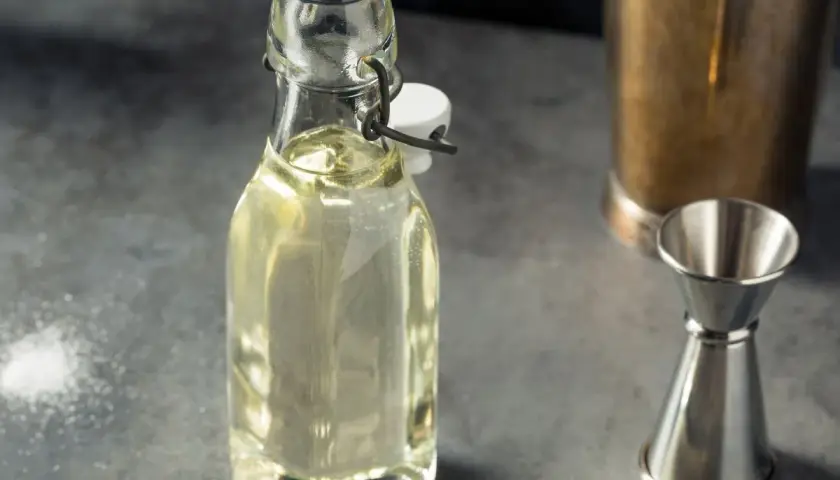 Domowy syrop cukrowy (simple syrup) w butelce, obok jigger i shakera. Idealny do drinków, łatwy do przygotowania krok po kroku.