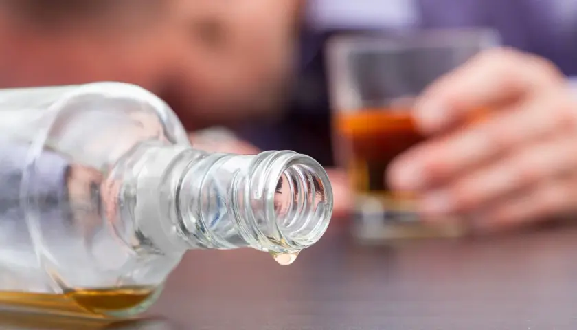Objawy zafałszowania alkoholu: jak rozpoznać metanol w domowej wódce? Kropla alkoholu z butelki, w tle osoba z kieliszkiem.