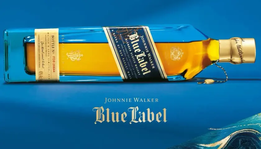 Elegancka butelka Johnnie Walker Blue Label leży na niebieskim tle. Złoty płyn i niebieskie szkło tworzą luksusowy kontrast.