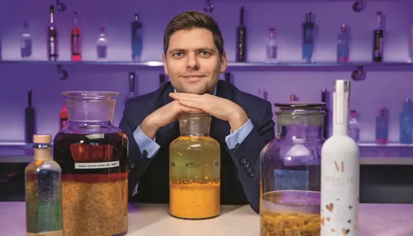 Ekspert prezentuje najlepsze techniki produkcji wódek rzemieślniczych (craft vodka), otoczony butelkami i słoikami z nalewami.