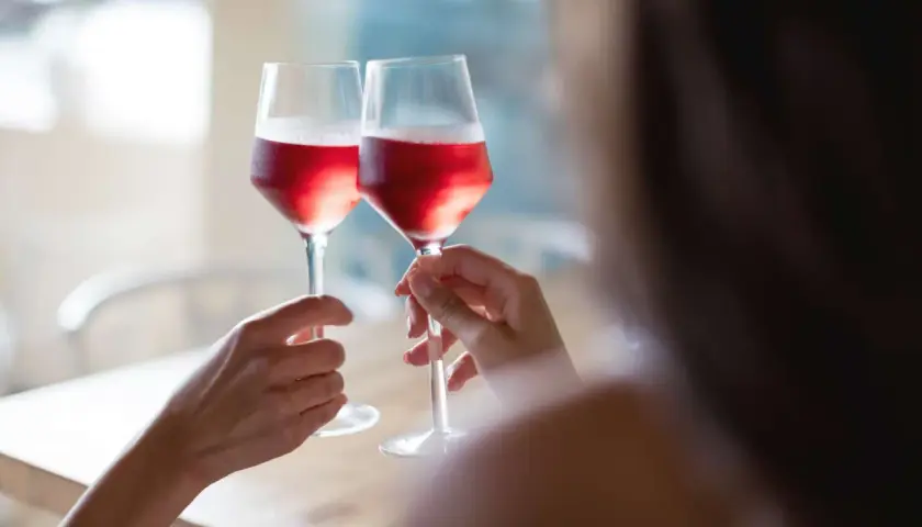 Dwie osoby wznoszą toast kieliszkami z różowym winem. Czy wino różowe powstaje z mieszania białego z czerwonym? Proces produkcji jest ciekawy!