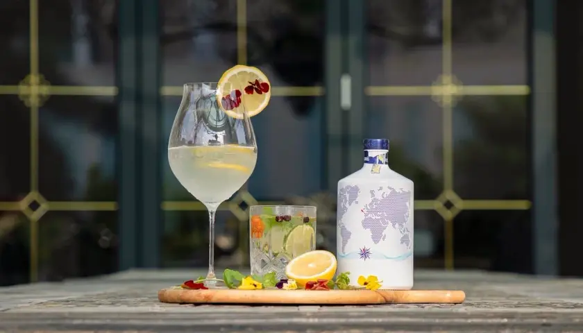 Jak przygotować infuzowany alkohol, np. wódkę o smaku chilli? Na stole stoją drinki, cytryny, zioła i butelka z mapą świata.