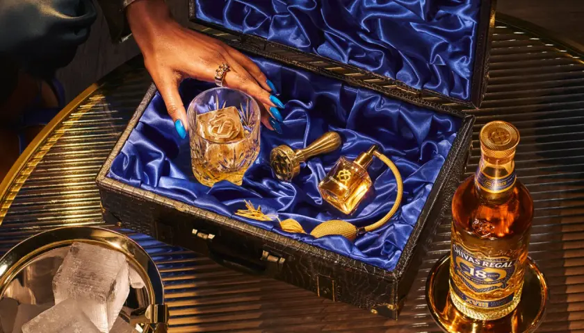 Skutki zbyt niskiej temperatury serwowania: dlaczego nie mrozić whisky. Elegancki zestaw z butelką Chivas Regal 18, szklanką z lodem i złotymi akcesoriami.