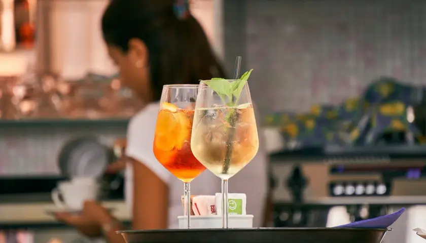 Dwa drinki: pomarańczowy Aperol Spritz i jasny Hugo. Różnica między aperol spritz a hugo w składnikach i kaloryczności jest widoczna.