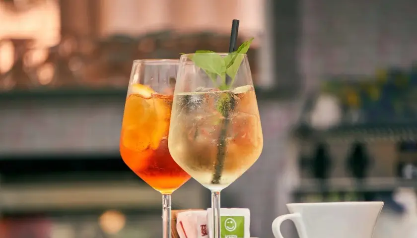 Dwa drinki z lodem i owocami, jeden pomarańczowy, drugi jasny. Czy warto kupować drogie giny do drinków mieszanych z owocami?
