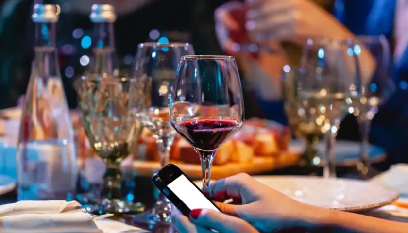 Zanim sięgniesz po alkohol, pomyśl o "podkładzie". Na stole wino, przekąski i telefon. Unikaj skutków picia alkoholu na pusty żołądek.