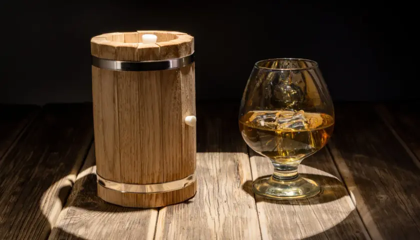 Mała beczka (quarter cask) i kieliszek whisky. Pokazuje skutki starzenia whisky w małych beczkach, przyspieszony proces.