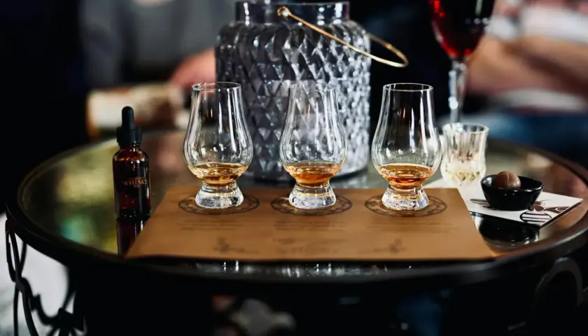 Degustacja whisky metodą tulipana: jak poczuć torf, wanilię i dym. Na stole kieliszki, buteleczka z whisky i czekoladka.